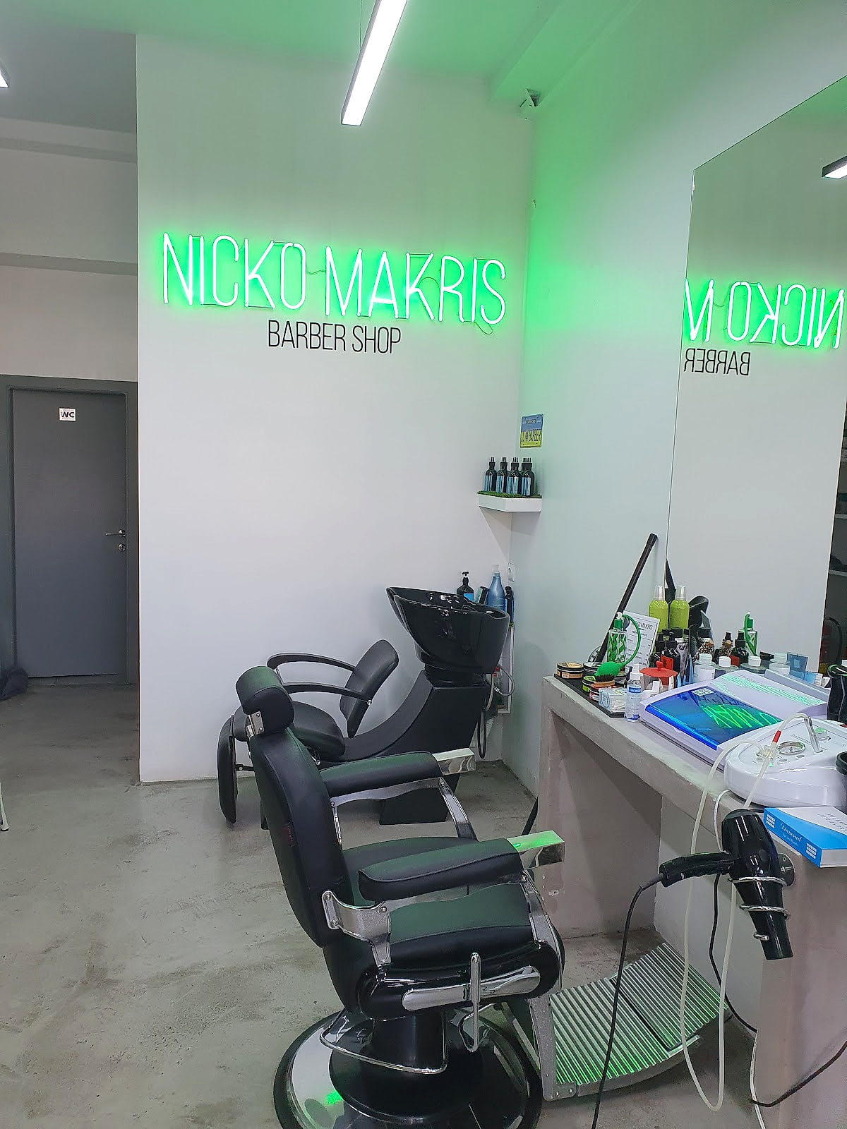 Ο τοίχος με το πράσινο neon «NICKO MAKRIS BARBER SHOP» μέσα στο μαγαζί.